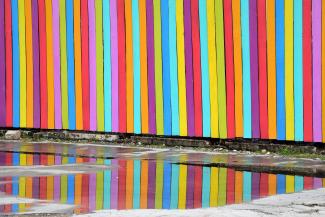 Fence with many colored slats reflected in a puddle