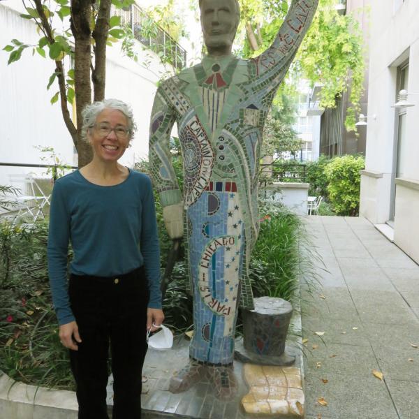 Portrait of Daisy Delogu standing in front of a whimsical statue of a human figure on the sidewalk in Paris, France