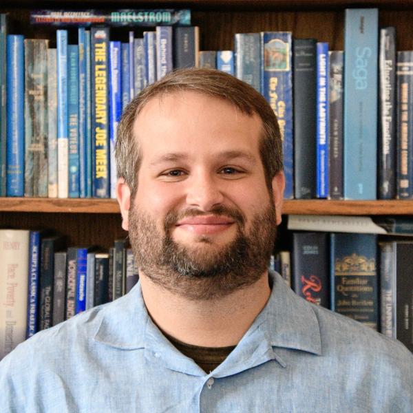 Portrait of Andrew Pitel in front of the MAPH Student Lounge bookshelf