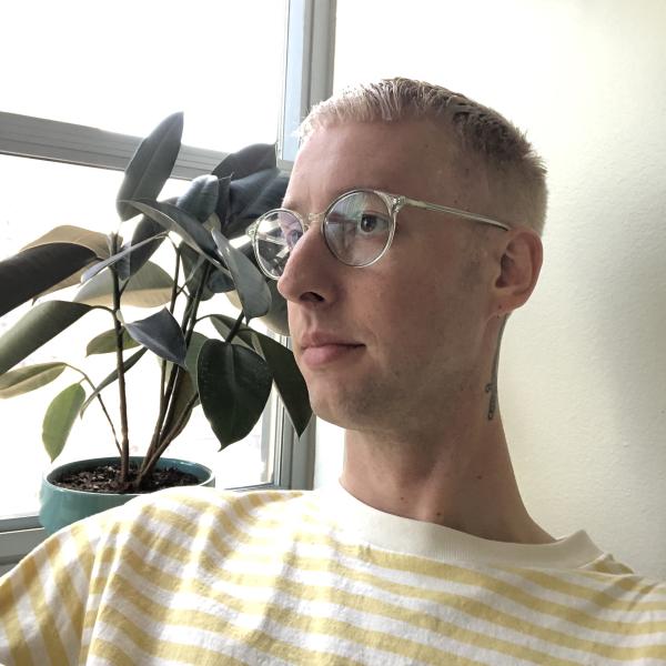 Portrait of Paul Goerner sitting next to a large window in front of a two houseplants