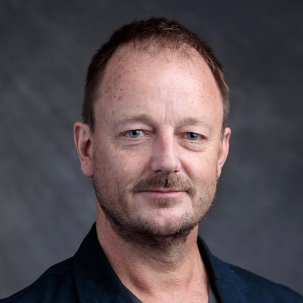 Portrait of Mark Payne in front of a grey wall