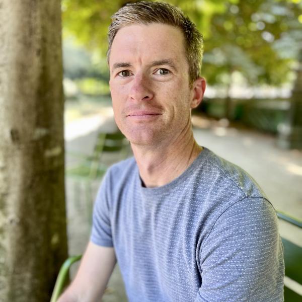Portrait of Ryan Van Meter sitting outside in front of green foliage