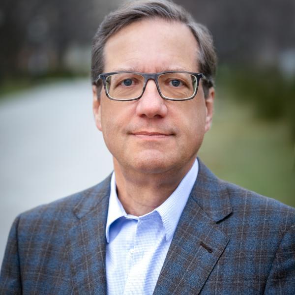 Portrait of David Schoen outside on UC campus in front of a blurred sidewalk and lawn