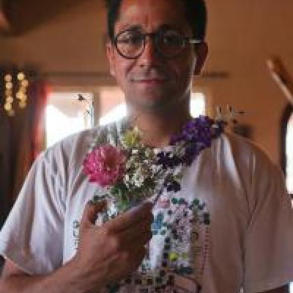 Portrait of Edgar Garcia standing inside in front of a paneled window and holding a bouquet of pink and purple flowers
