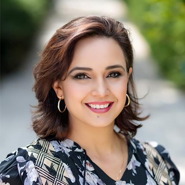 Portrait of Verónica Moraga outside on UC campus in front of a concrete walkway and trees