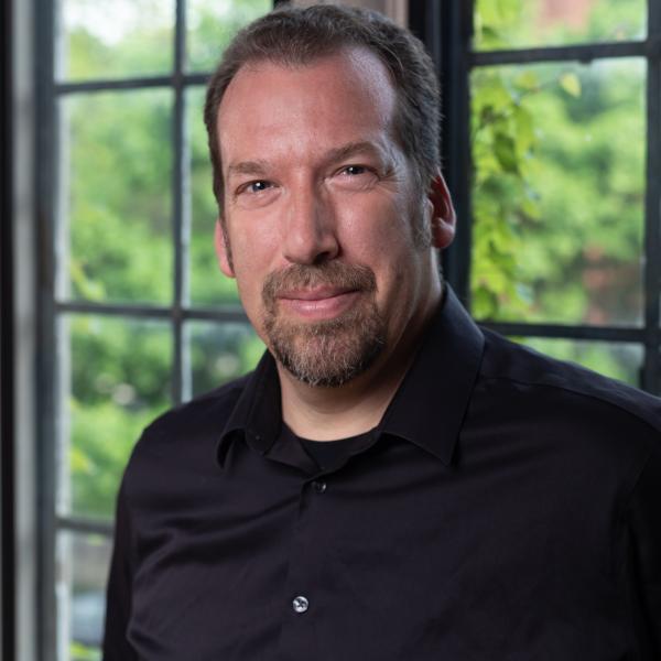 Portrait of Dan Morgan standing in front of a large paneled window indoors at UChicago