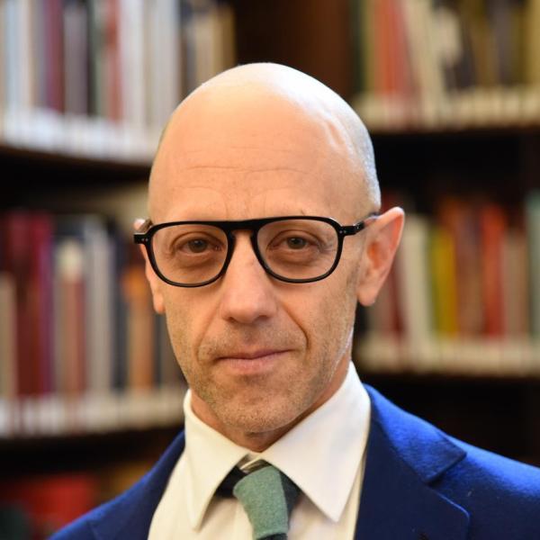 Portrait of Justin Steinberg standing in front of a bookshelf inside UChicago