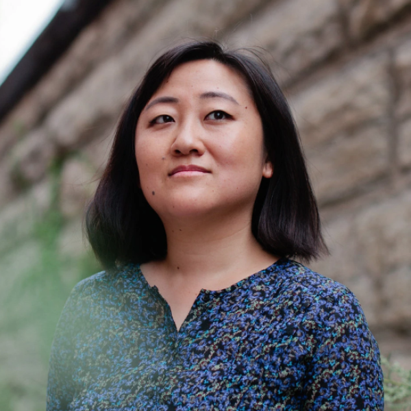 Portrait of Ling Ma standing outside in front of a stone wall with a blurry leaf in the foreground