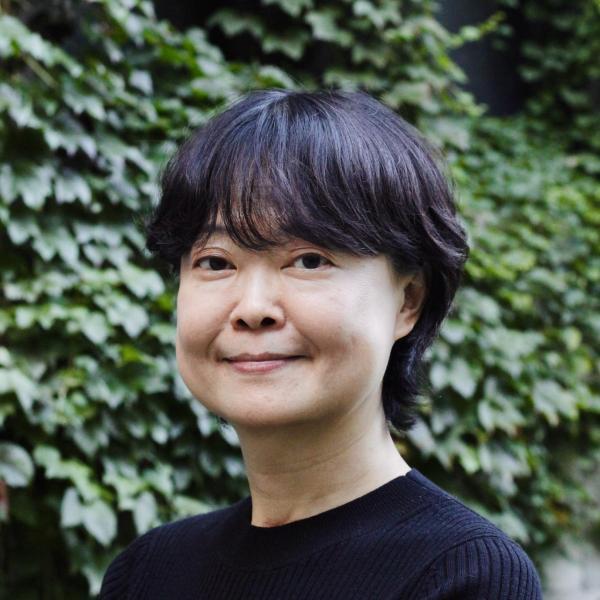 Portrait of Ming Xiang outdoors from the shoulders up in front of an ivy covered wall